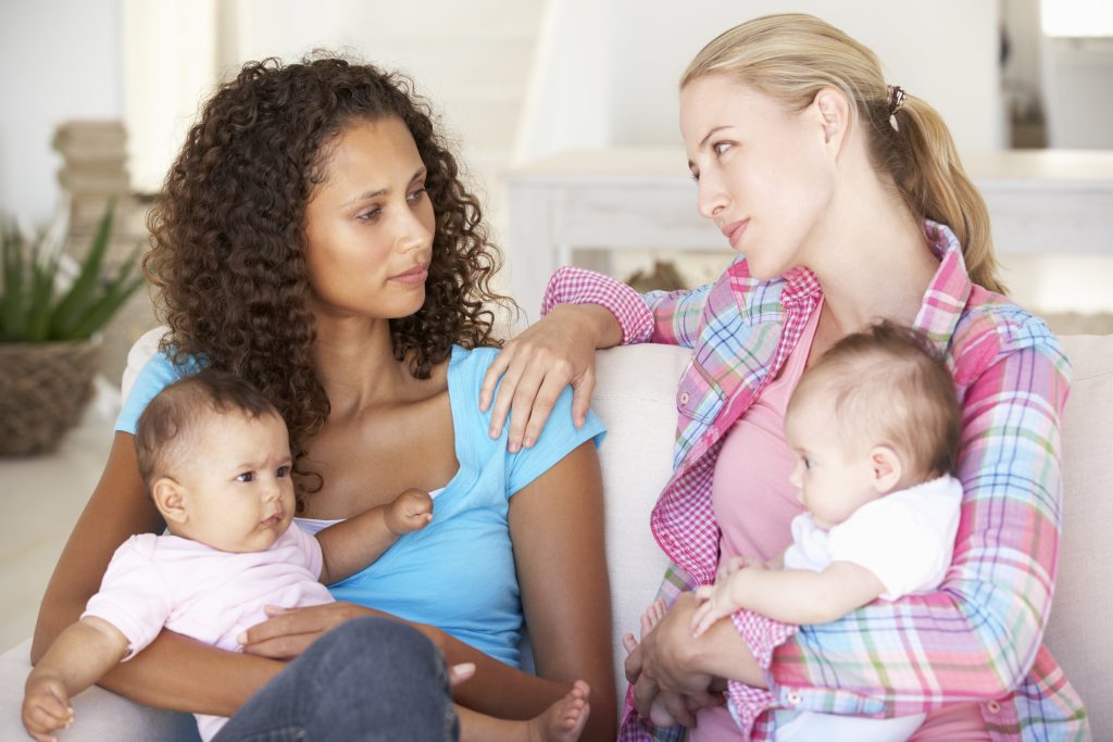 Two Young Mothers On Sofa At Home