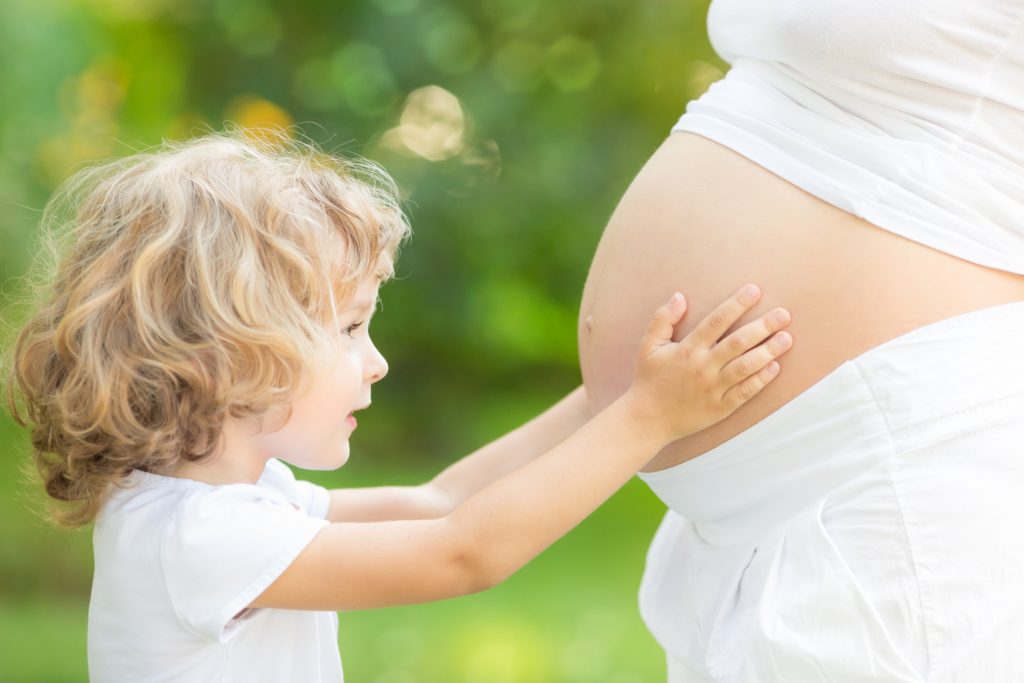 Happy child holding belly of pregnant woman against green spring background