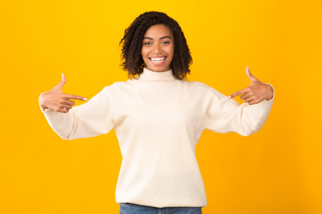 Clothes Template. Happy black woman pointing at white pullover hoodie, mockup for logo or branding design