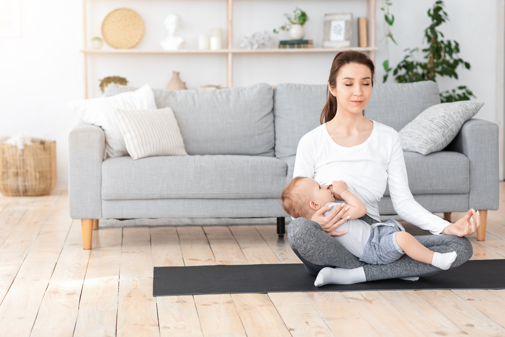 Coping With Motherhood Stress. Young Mom Breastfeeding Baby And Meditating At Home, Sitting In Lotus Position Of Floor, Copy Space