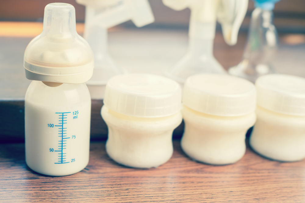 BABY BOTTLE WITH MILK AND A MEASURING SCALE, MANUAL BREAST PUMP, MOTHERS BREAST MILK IS THE MOST HEALTHY FOOD FOR NEWBORN BABY. OBJECTS STANDING IN A ROW. SELECTIVE FOCUS